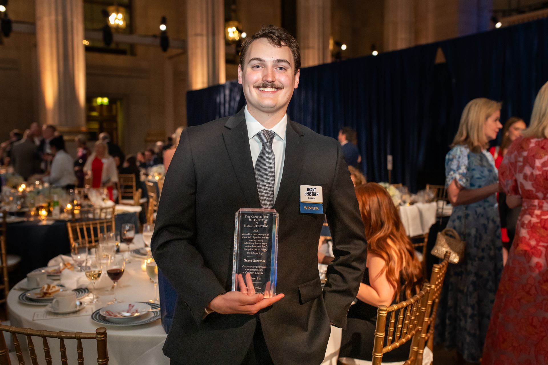 Man in a suit holding a trophy at a formal banquet event