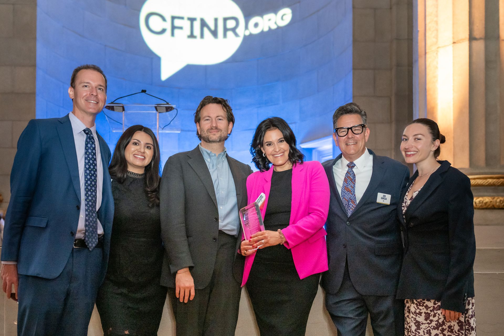 Six people posing at a CFINR.org event, with a blue backdrop and a speech bubble logo.
