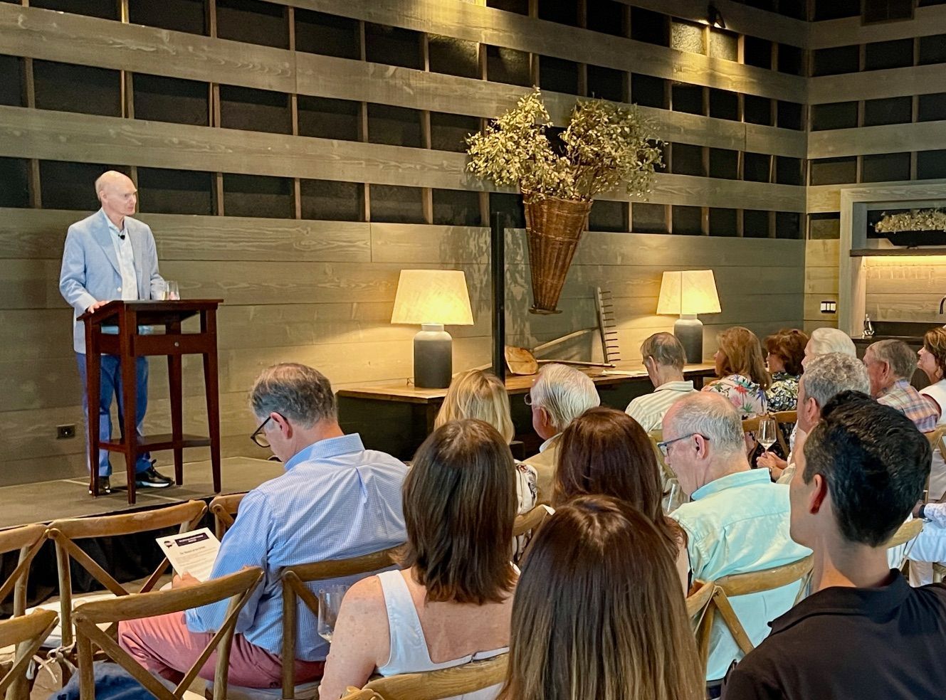 A man is standing at a podium giving a speech to a group of people sitting in chairs.