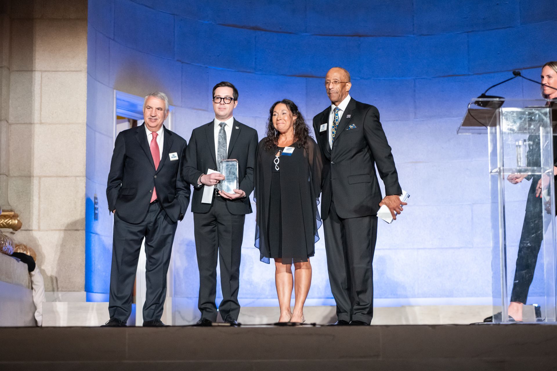 Four people onstage posing with awards at a formal ceremony under blue lighting
