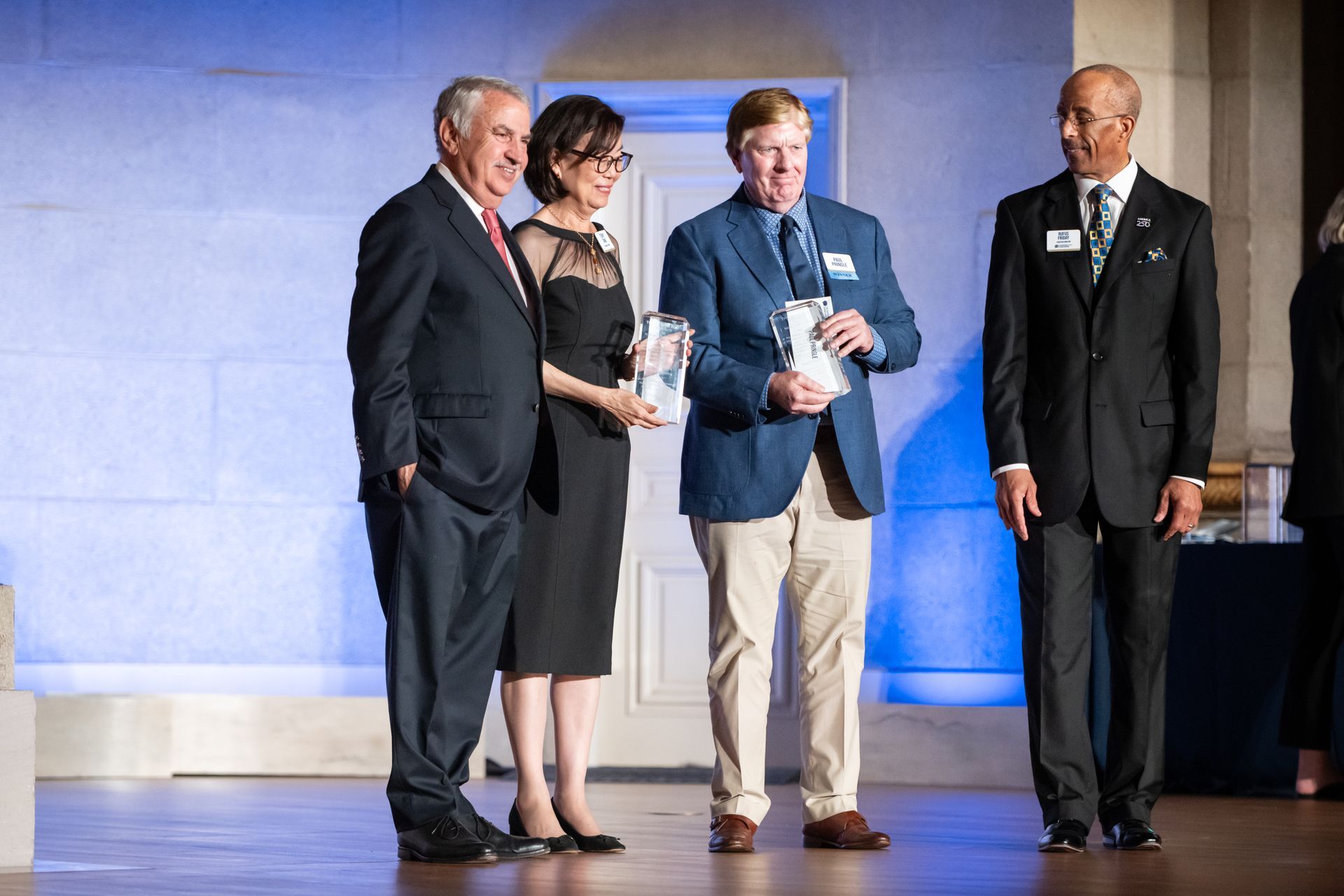 Four people stand on a stage under blue lighting, with one man holding an award or plaque.