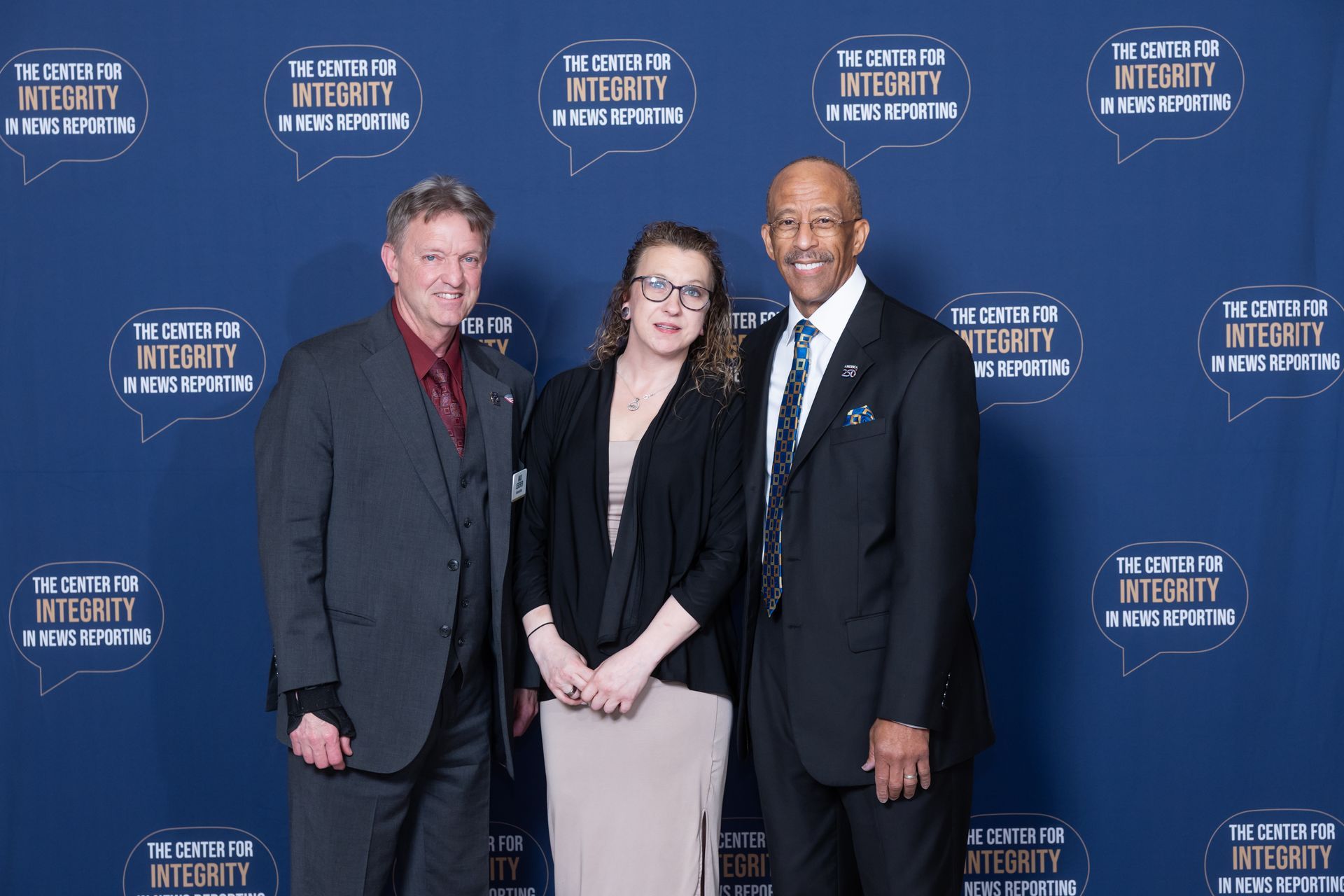 Three people posing in front of a blue event backdrop with repeated white logos.