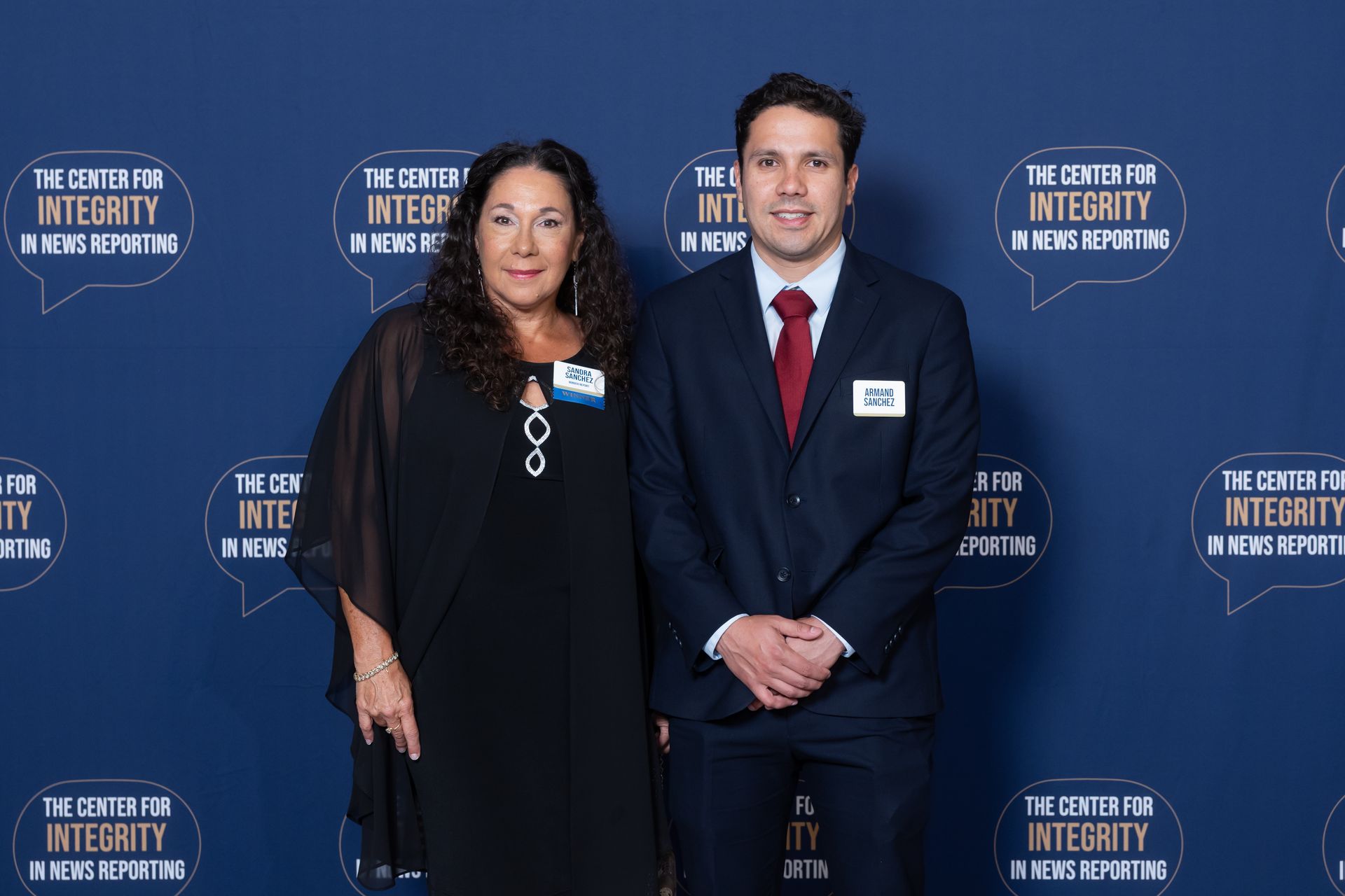 Two people posing in formal attire at The City of Integrity event backdrop.