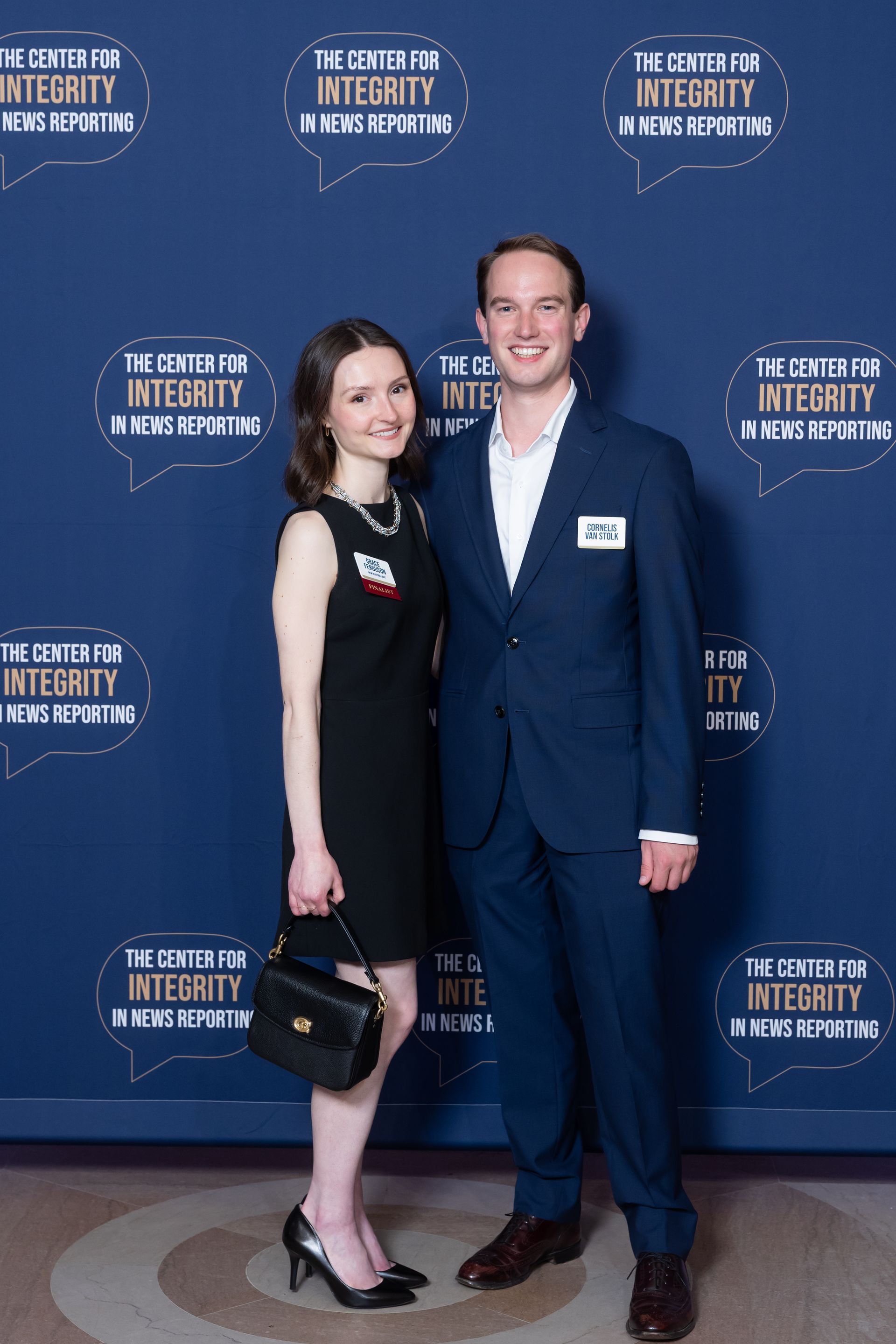 Couple posing at a step-and-repeat event backdrop, dressed in formal attire.
