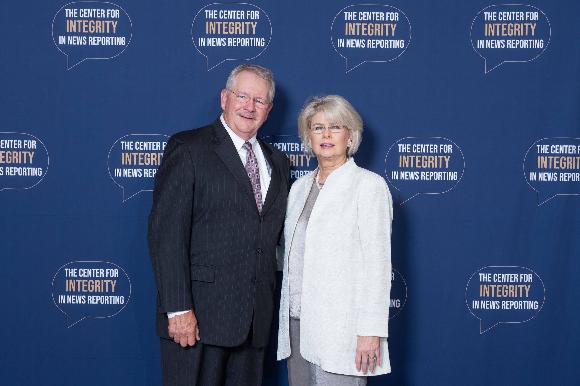 Two people posing in formal attire before a blue event backdrop.