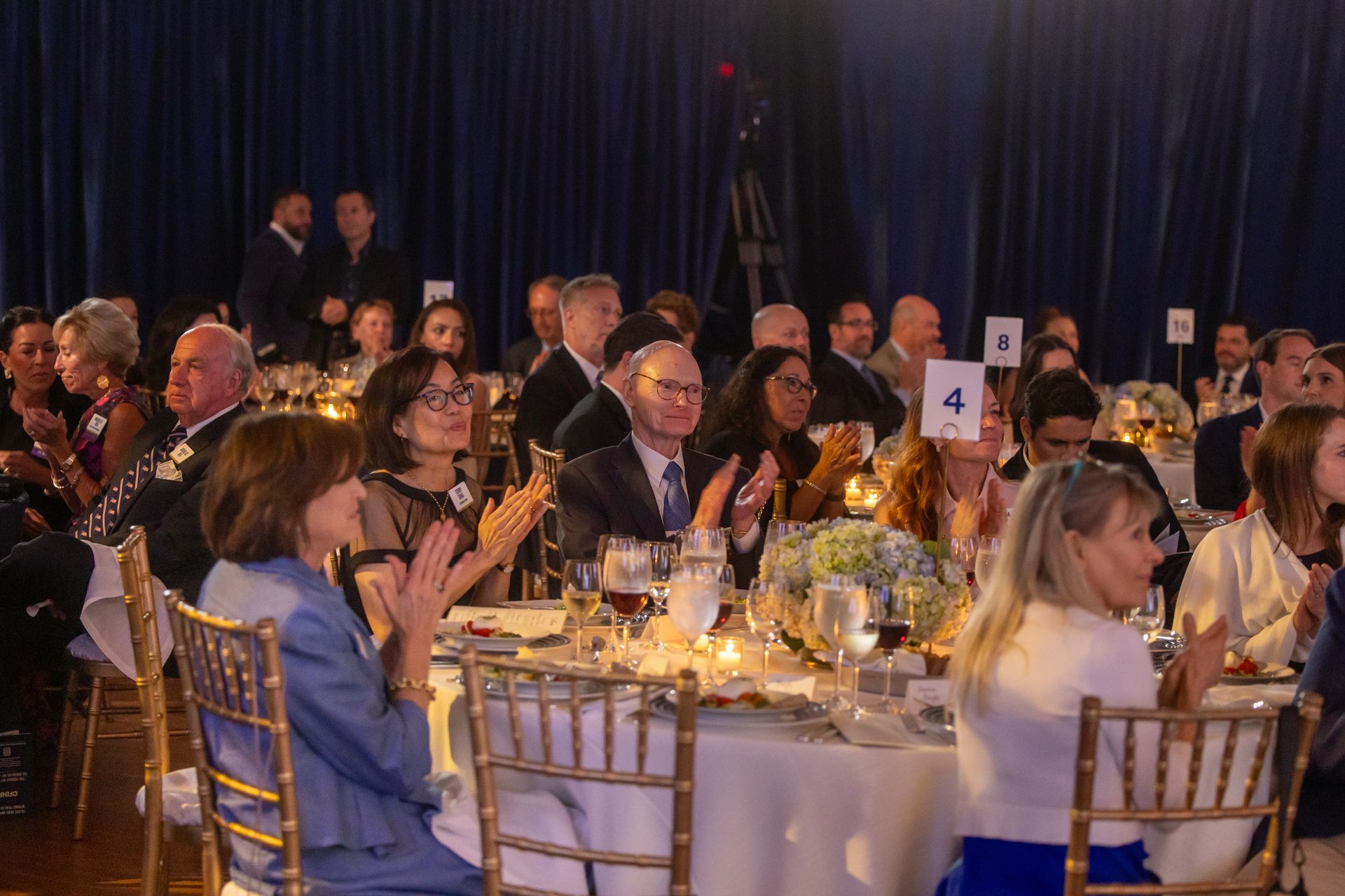 Guests applauding at a formal banquet with round tables and candlelit centerpieces
