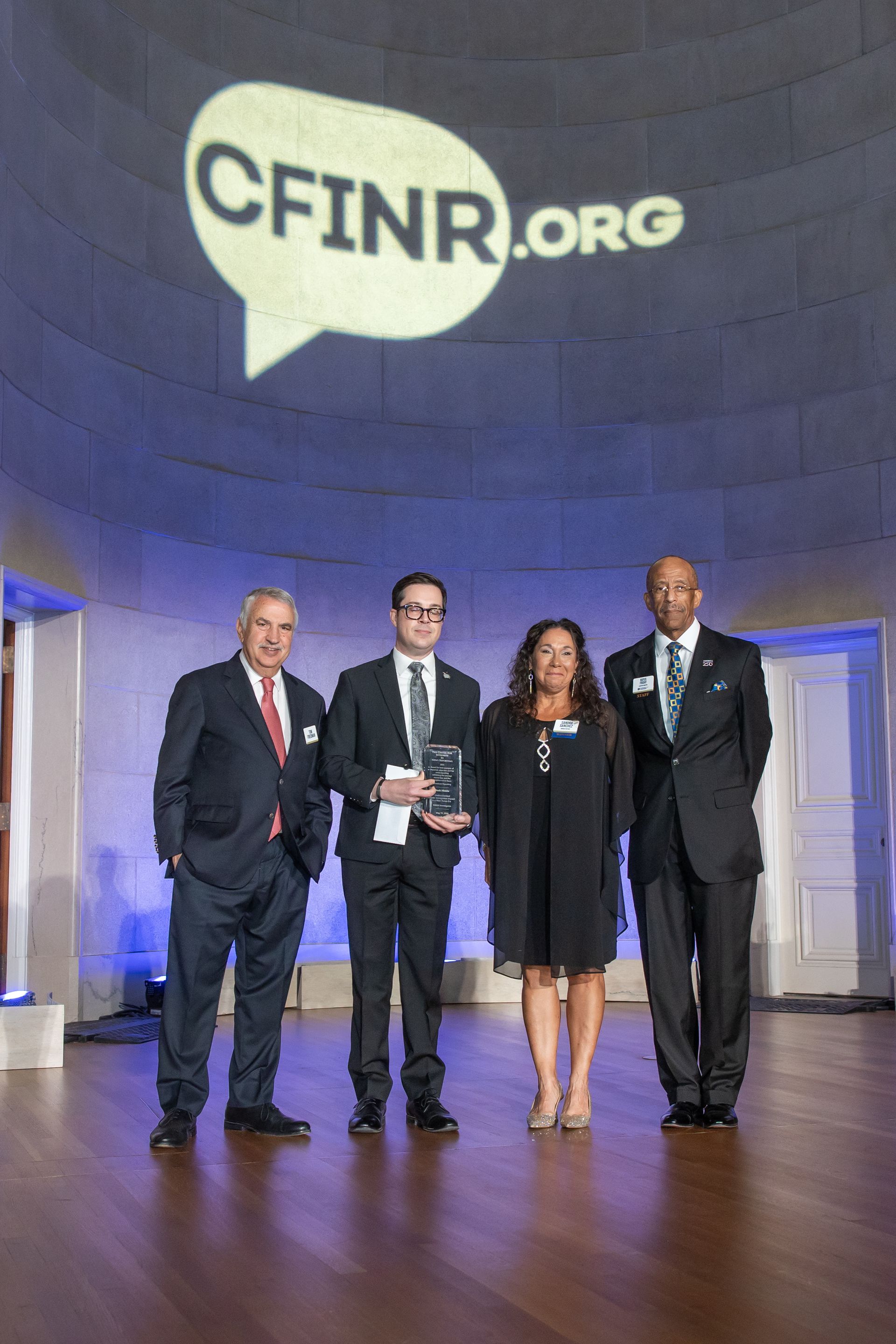 Four people posing onstage under a large CFINR.org projection