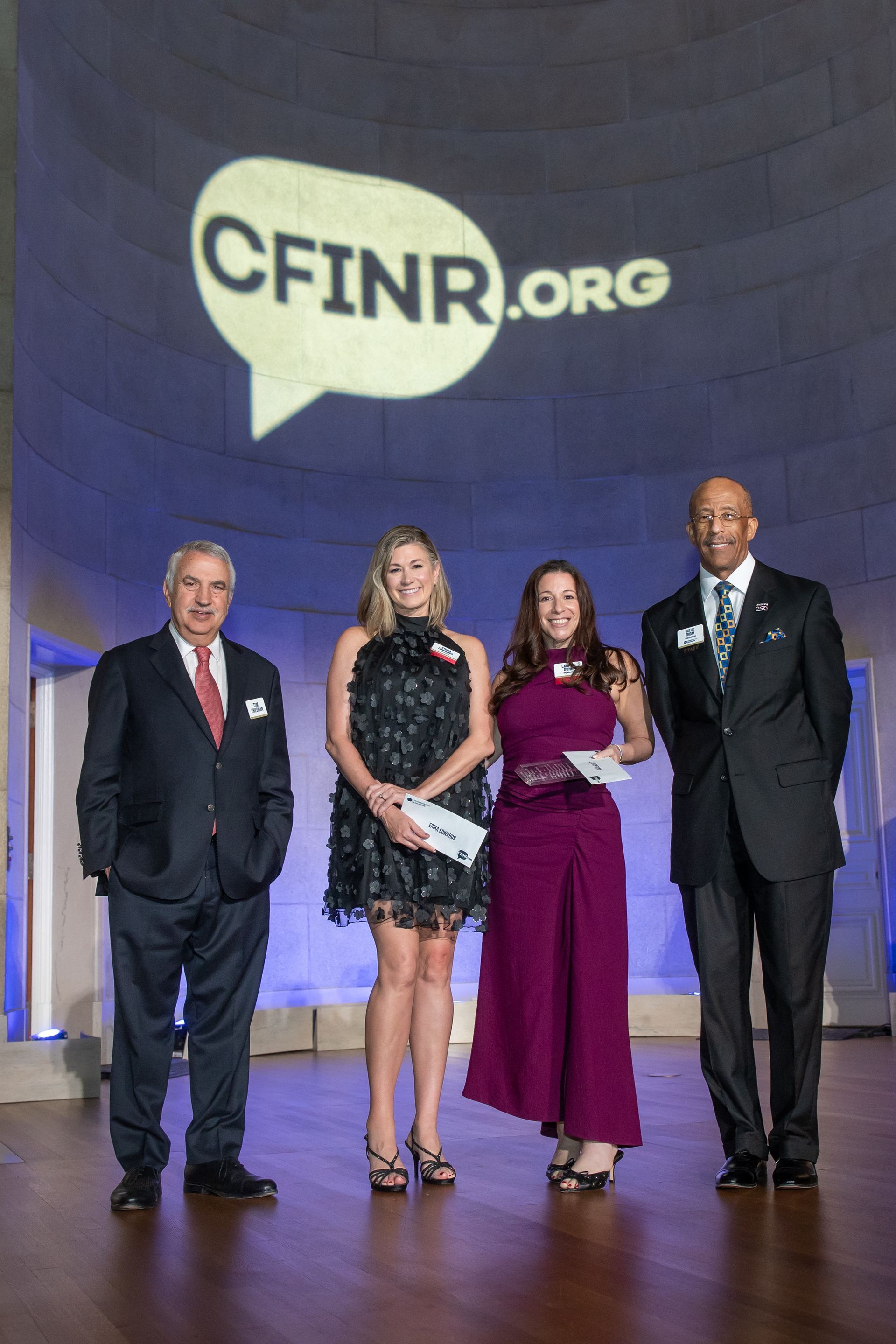 Four people stand on a stage before a CFINR.org backdrop, dressed in formal attire.