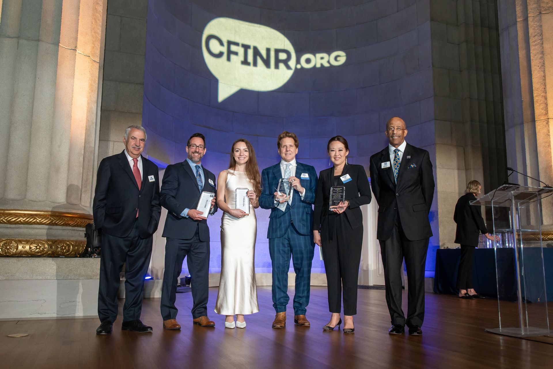 Six people stand onstage at a CFINR.org event, with a large logo projected behind them.