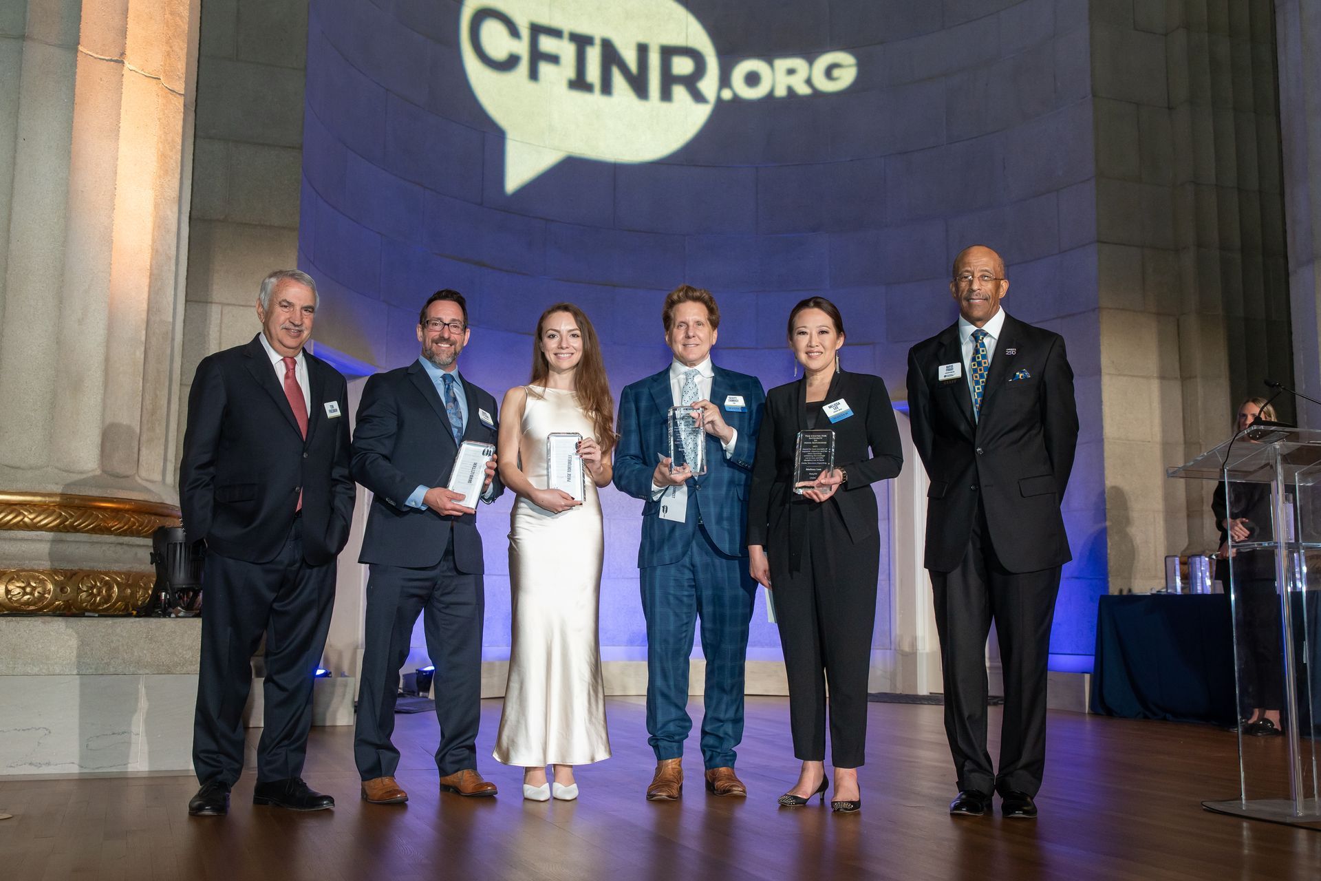 Six people on a stage holding awards in front of a large CFINR.org screen