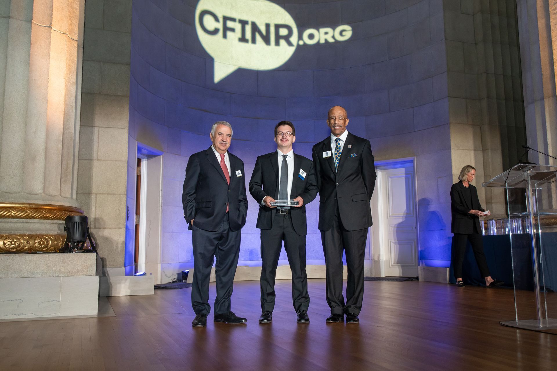 Three men in suits pose on stage beneath a CFINR.org banner at an awards ceremony.