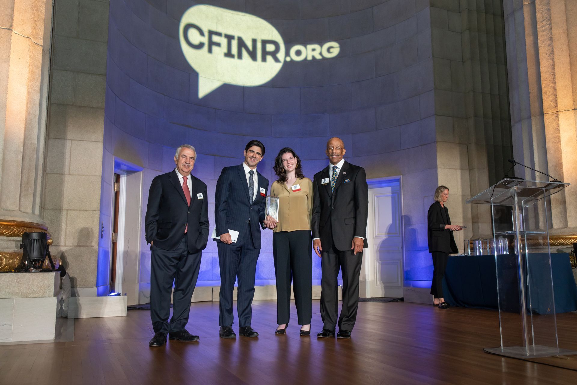 Four people on a lit stage beneath a CFINR.org projection, standing for a formal event.