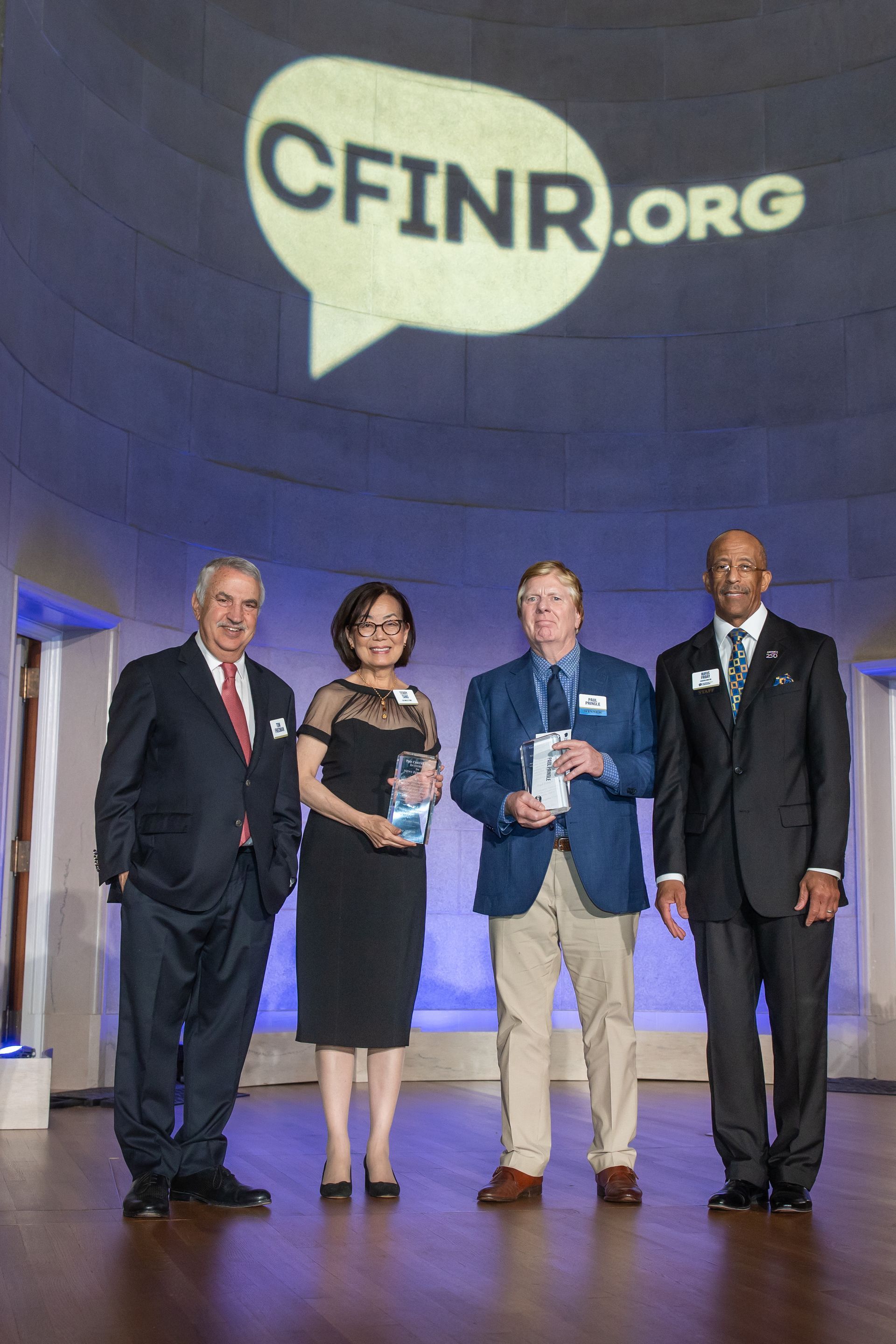 Four people on stage posing under a large CFINR.org logo, one holding an award plaque.