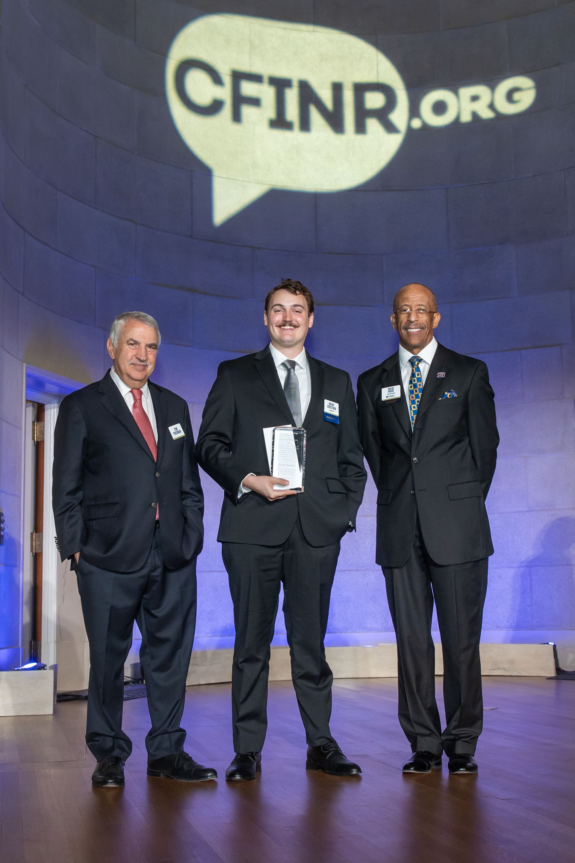 Three men in suits pose onstage beneath a CFINR.org backdrop.