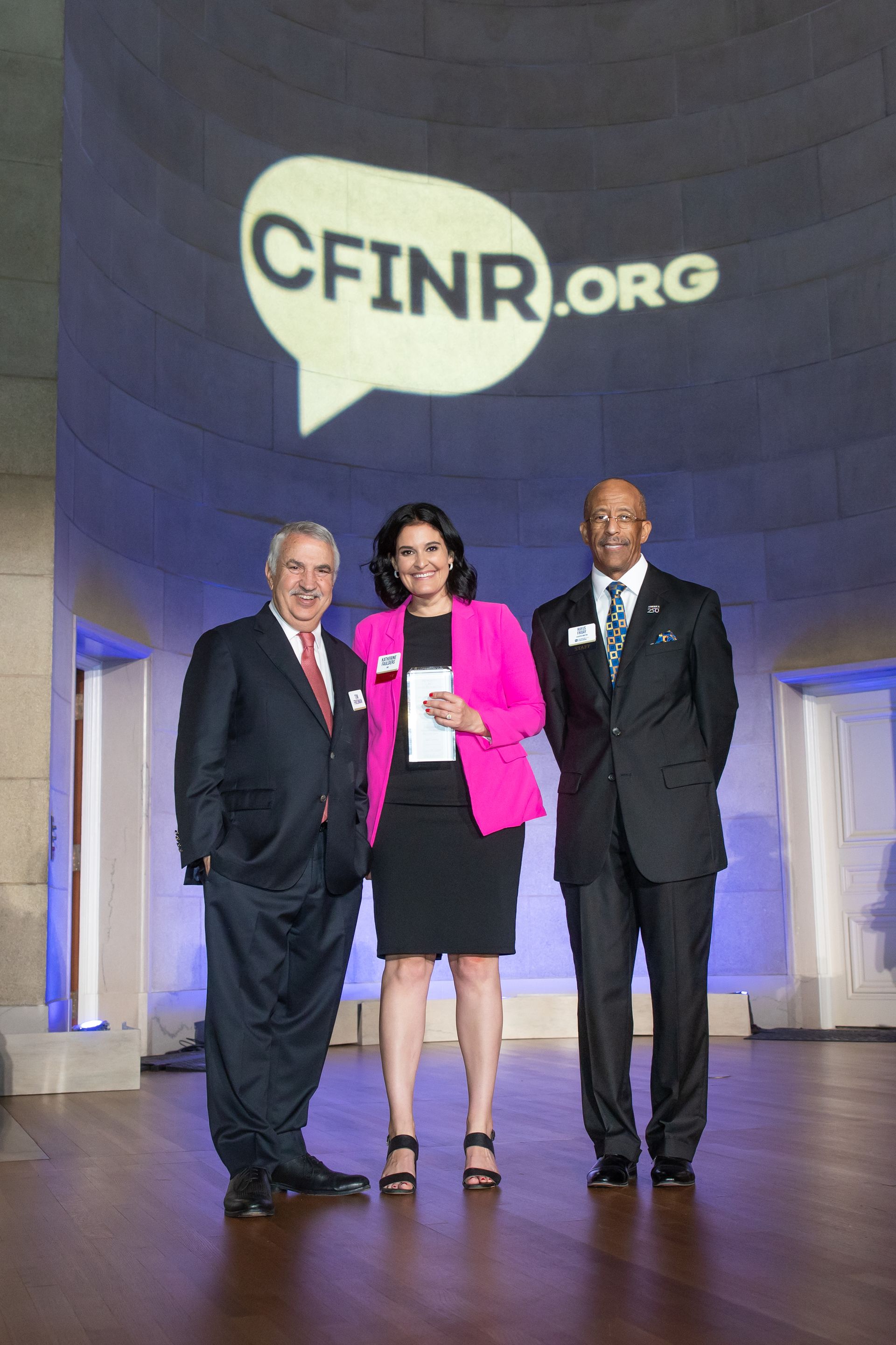 Three people standing on a stage beneath a large CFINR.org logo