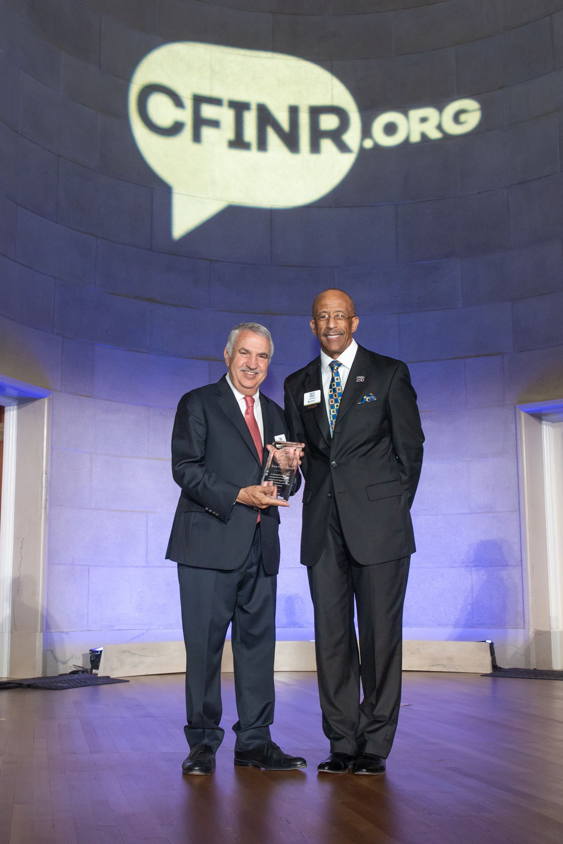 Two men in suits holding an award on a stage beneath a large CFINR.org sign.