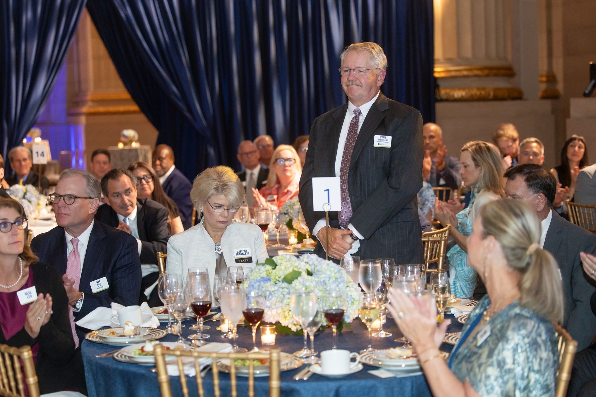Man speaking at a formal banquet table with seated guests and candles in a decorated ballroom