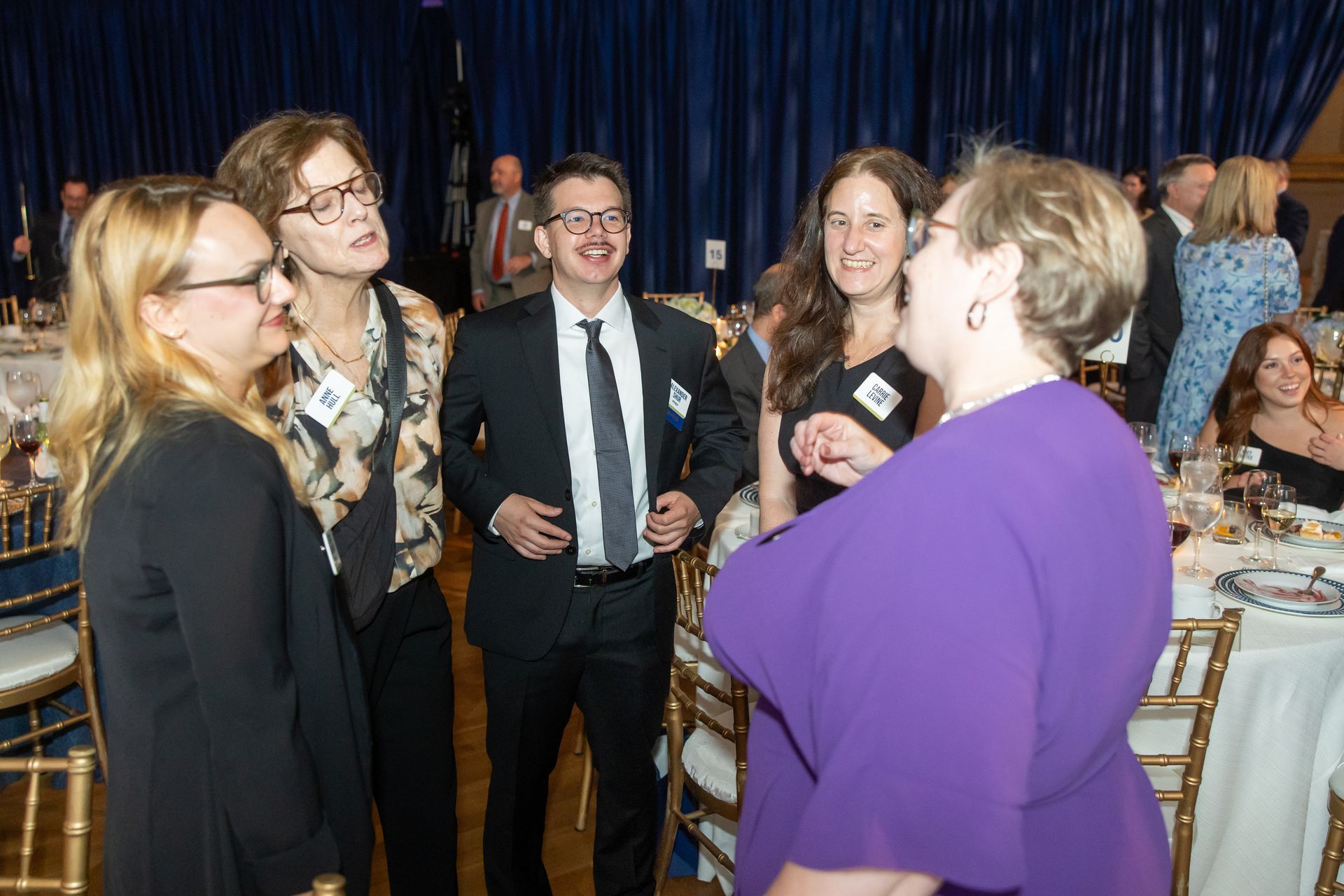 Four people in formalwear converse at a banquet table in a draped event hall.