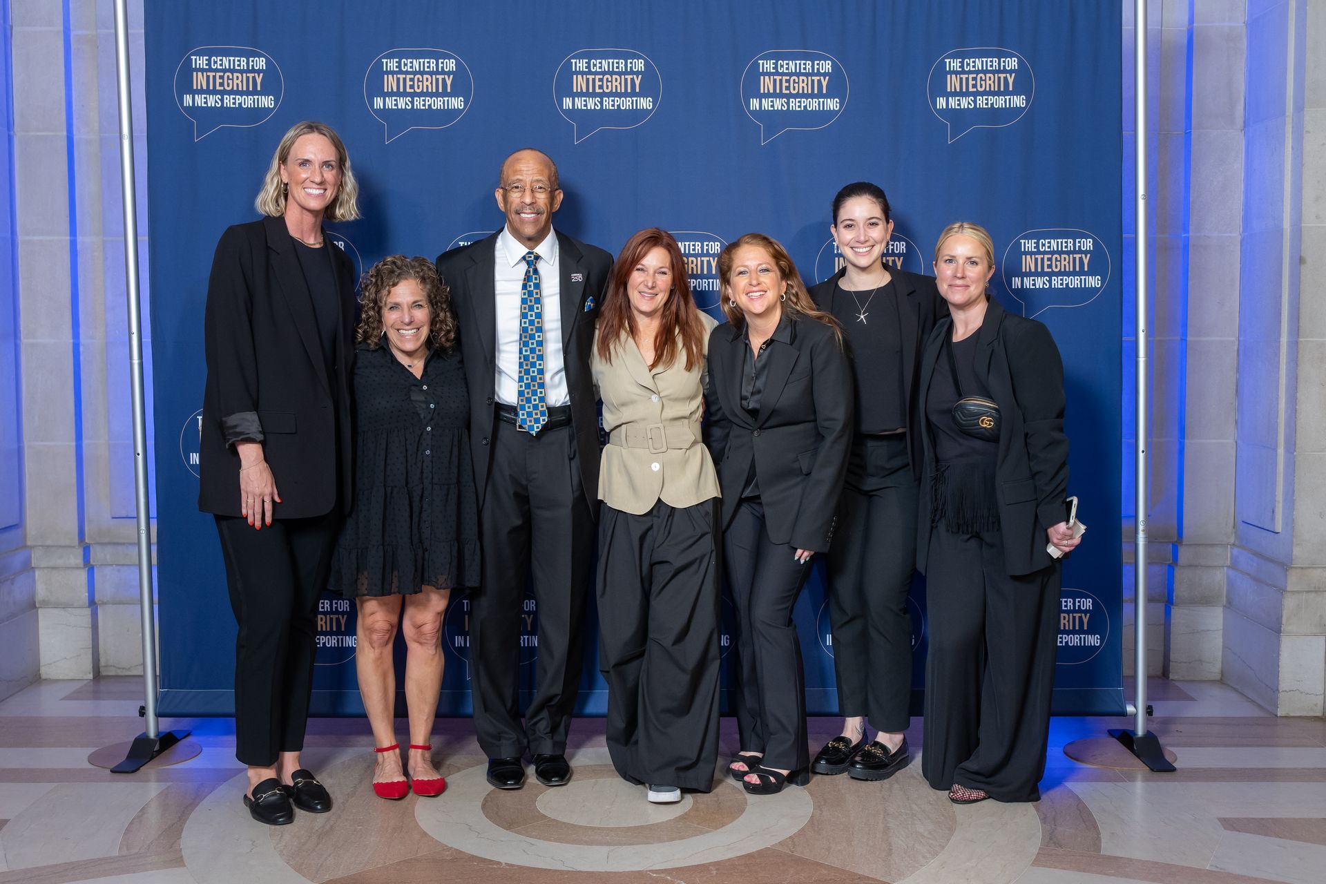Six people pose on a blue-carpet step-and-repeat backdrop at an awards event.