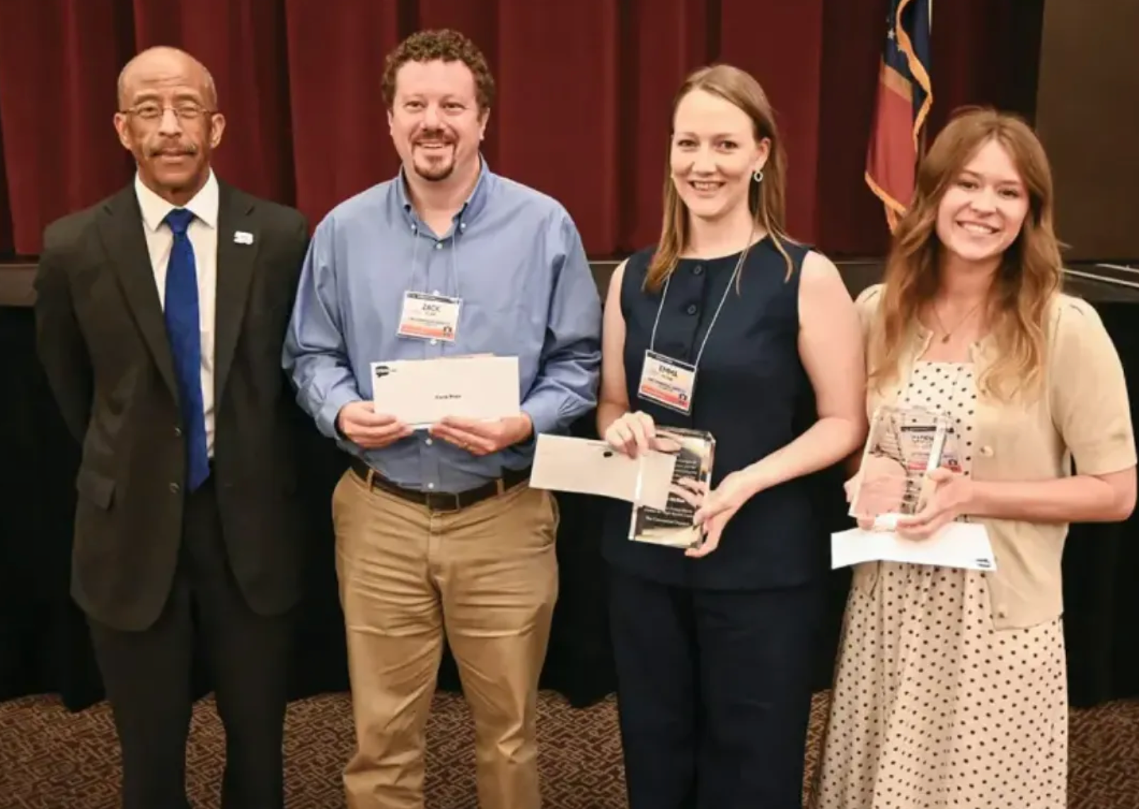 Four people pose with awards in front of a red curtain after a newspaper editorial honors ceremony