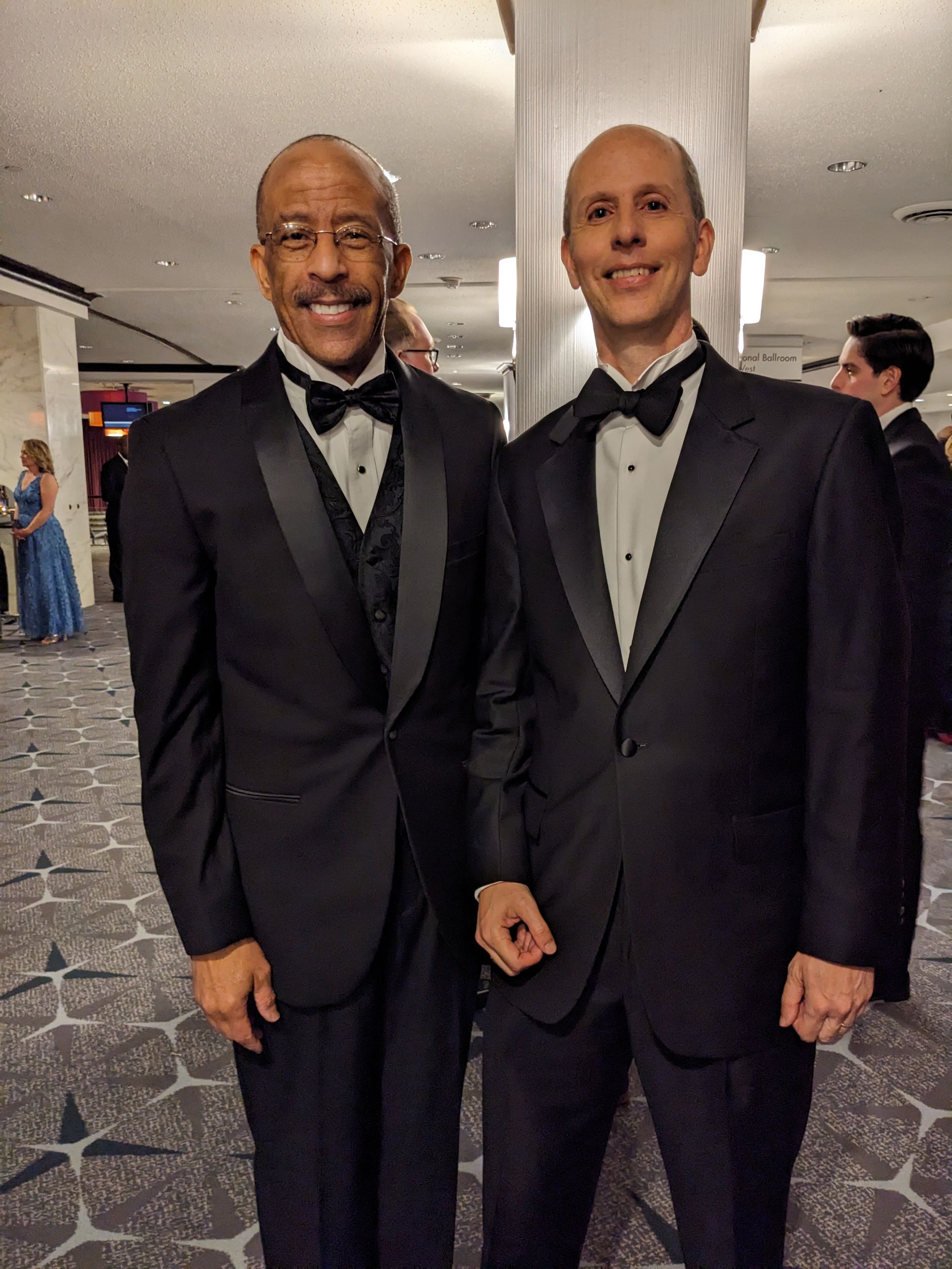 Two men in tuxedos and bow ties pose for a picture