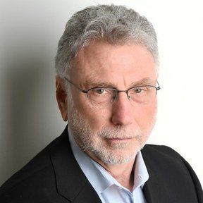 A man with a beard and glasses is wearing a suit and looking at the camera.