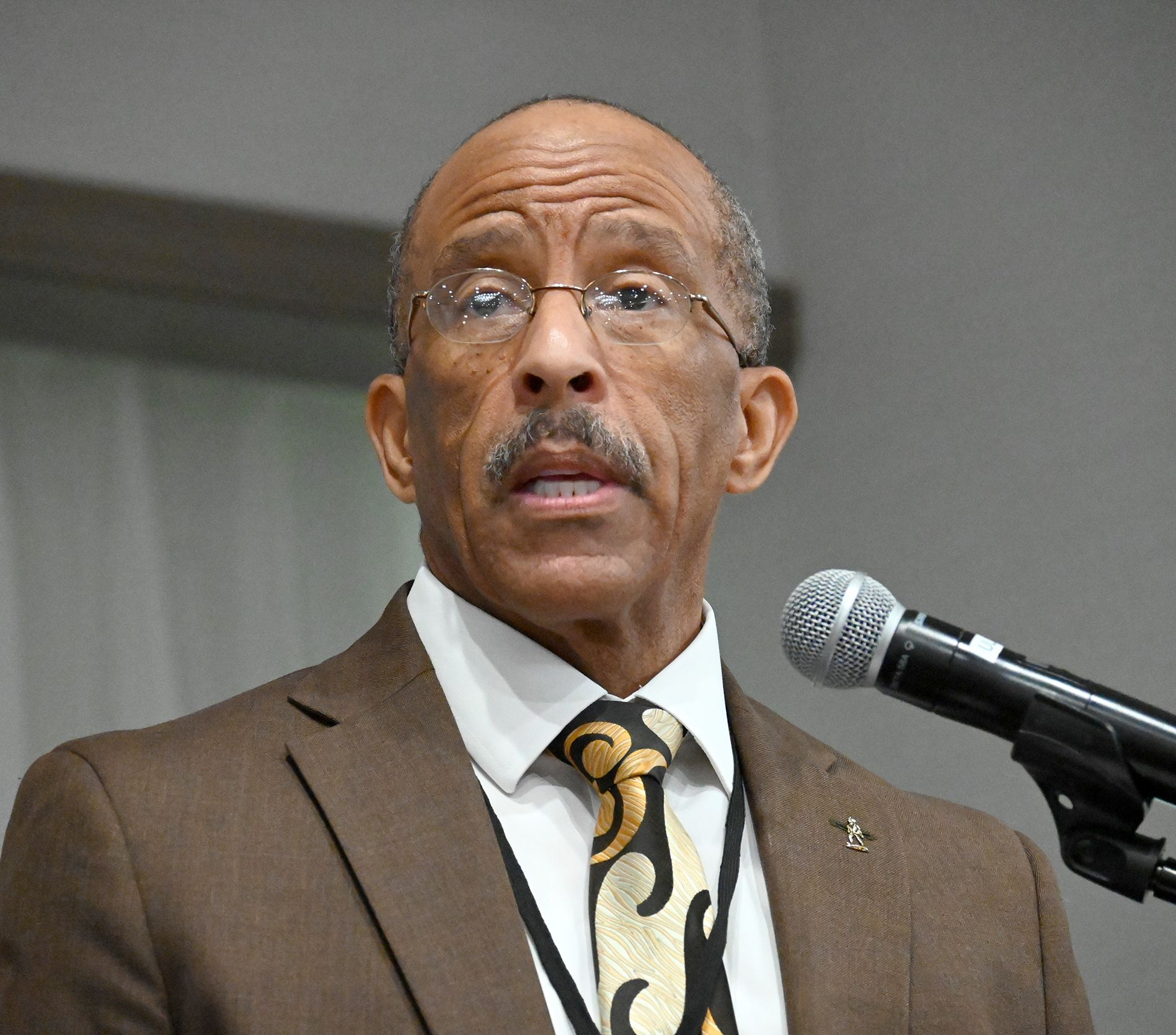 A man in a suit and tie is speaking into a microphone