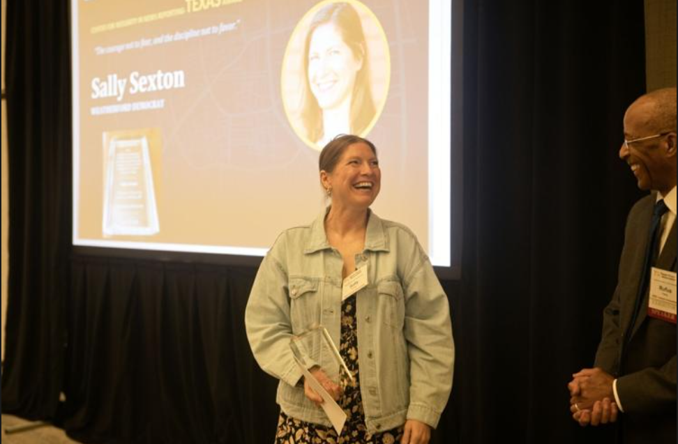 Two people smiling beside a projected presentation slide in a conference room