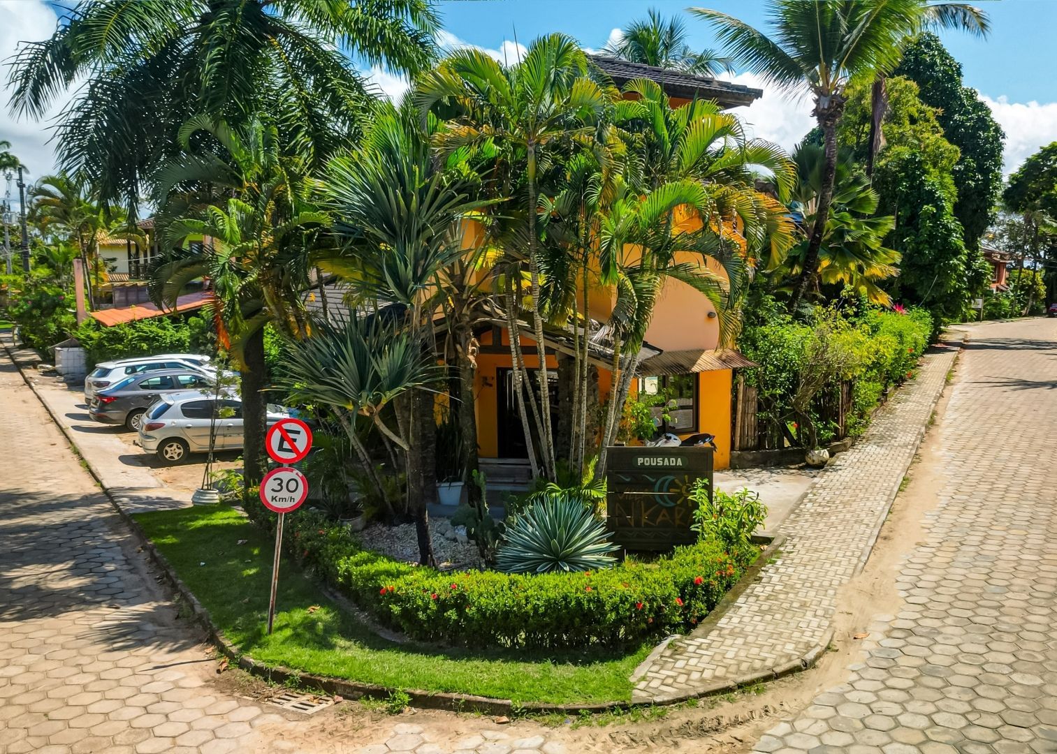 Um estacionamento com carros estacionados em frente a uma casa cercada por árvores e arbustos.