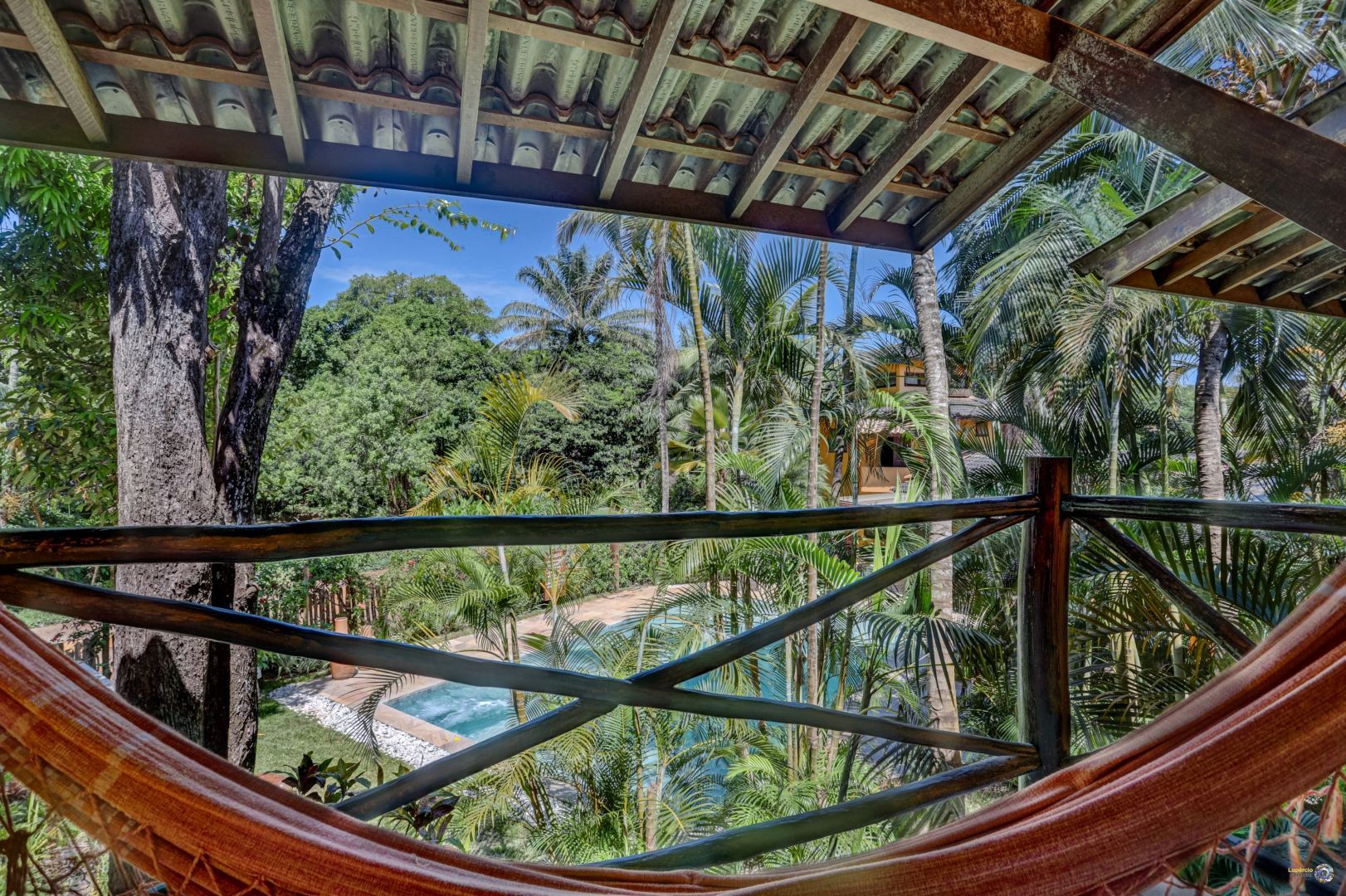 Uma rede está pendurada em uma grade de madeira com vista para uma floresta verdejante.
