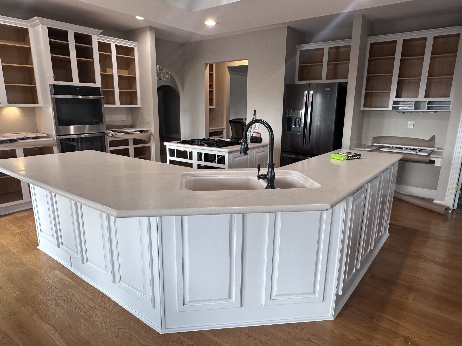 Modern white kitchen with large island, black appliances, and wood flooring