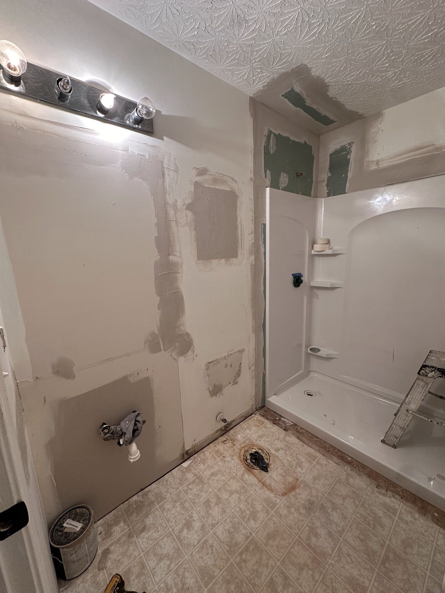 Empty bathroom under renovation with patched walls, a shower, sink, and unfinished floor.