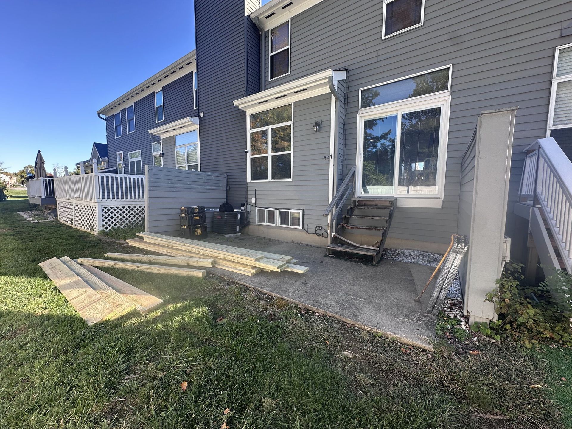 Back patio with steps, white railing, windows, and a concrete walkway beside a gray house