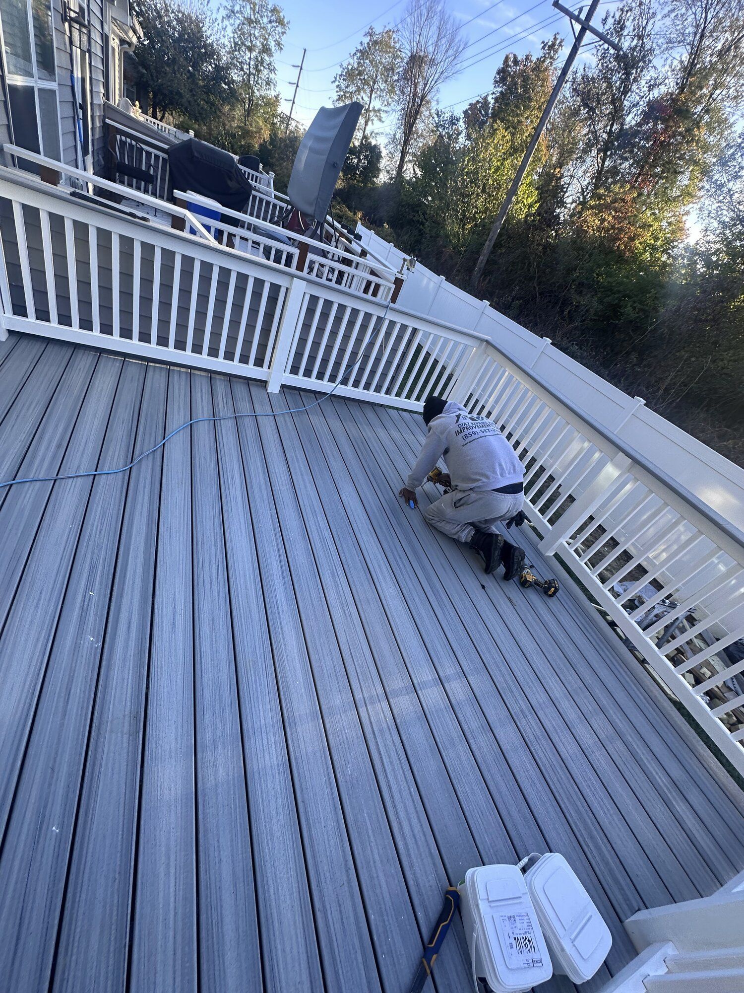 Person power washing a white deck with railings on a sunny day.