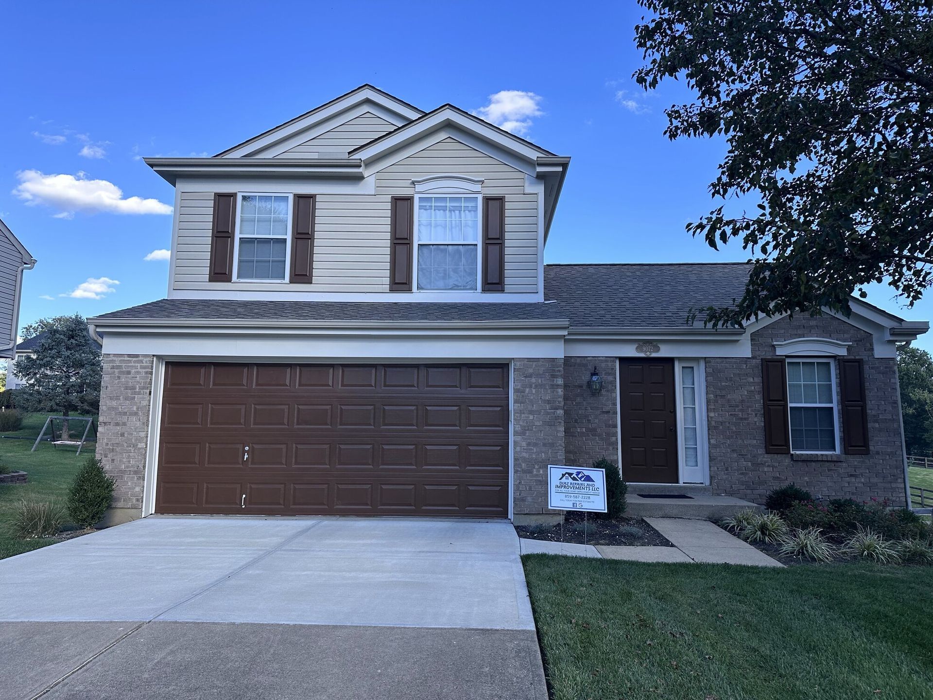 Suburban two-story house with brown garage, brick and siding exterior, and a front lawn under blue sky