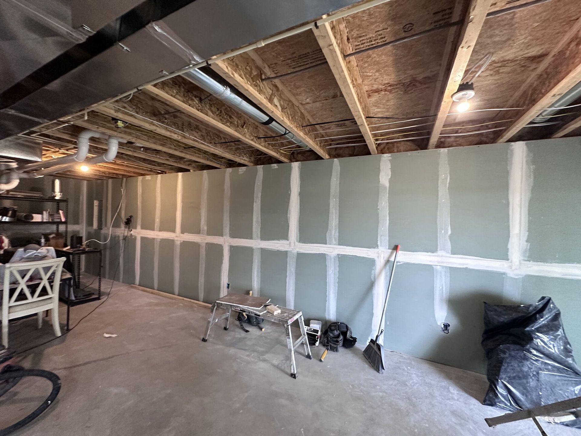 Unfinished basement with drywall, exposed ceiling joists, tools, and trash bags along the wall