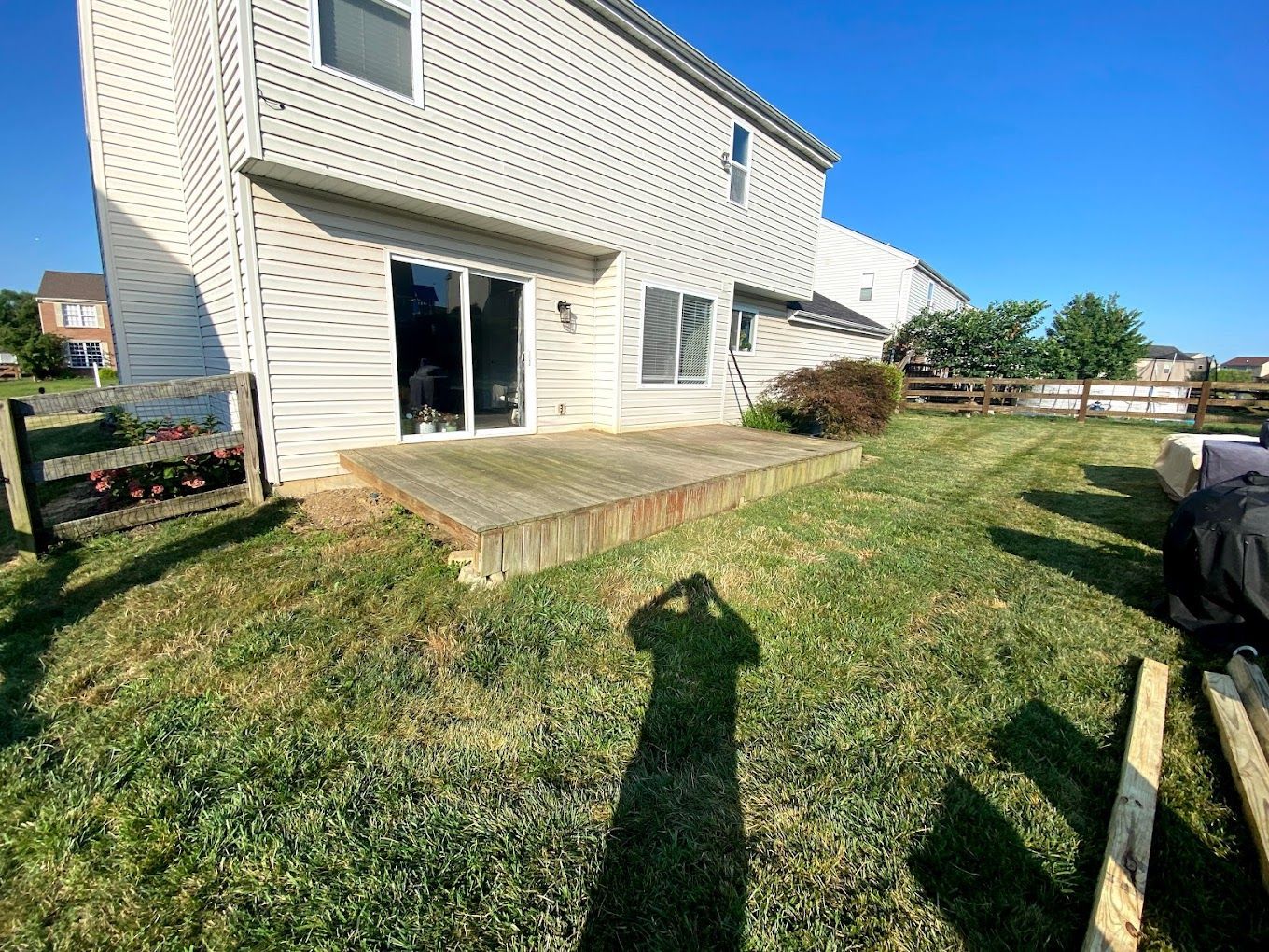A shadow of a person is cast on the grass in front of a house.