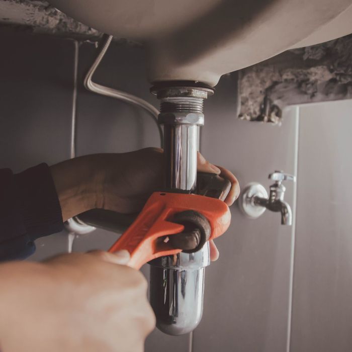 A person is fixing a sink with a wrench.