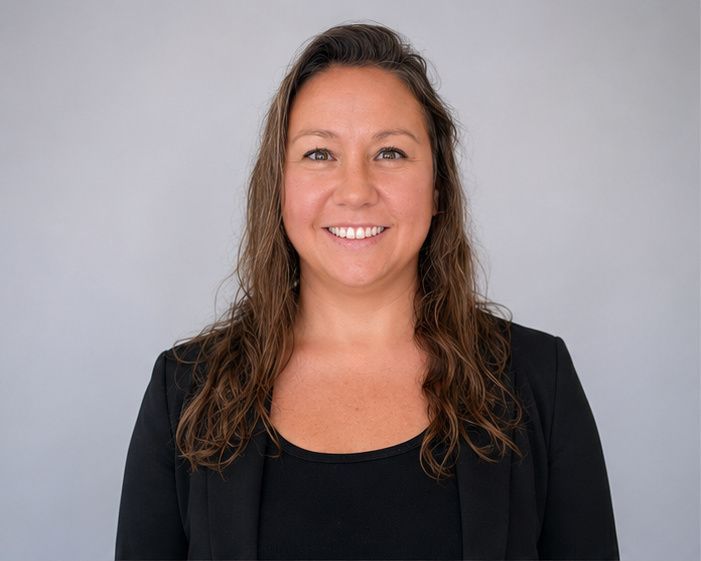 Smiling person in a black blazer against a light gray background.