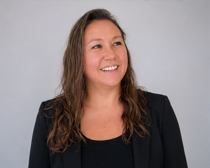 Smiling person in a black blazer against a light gray background.