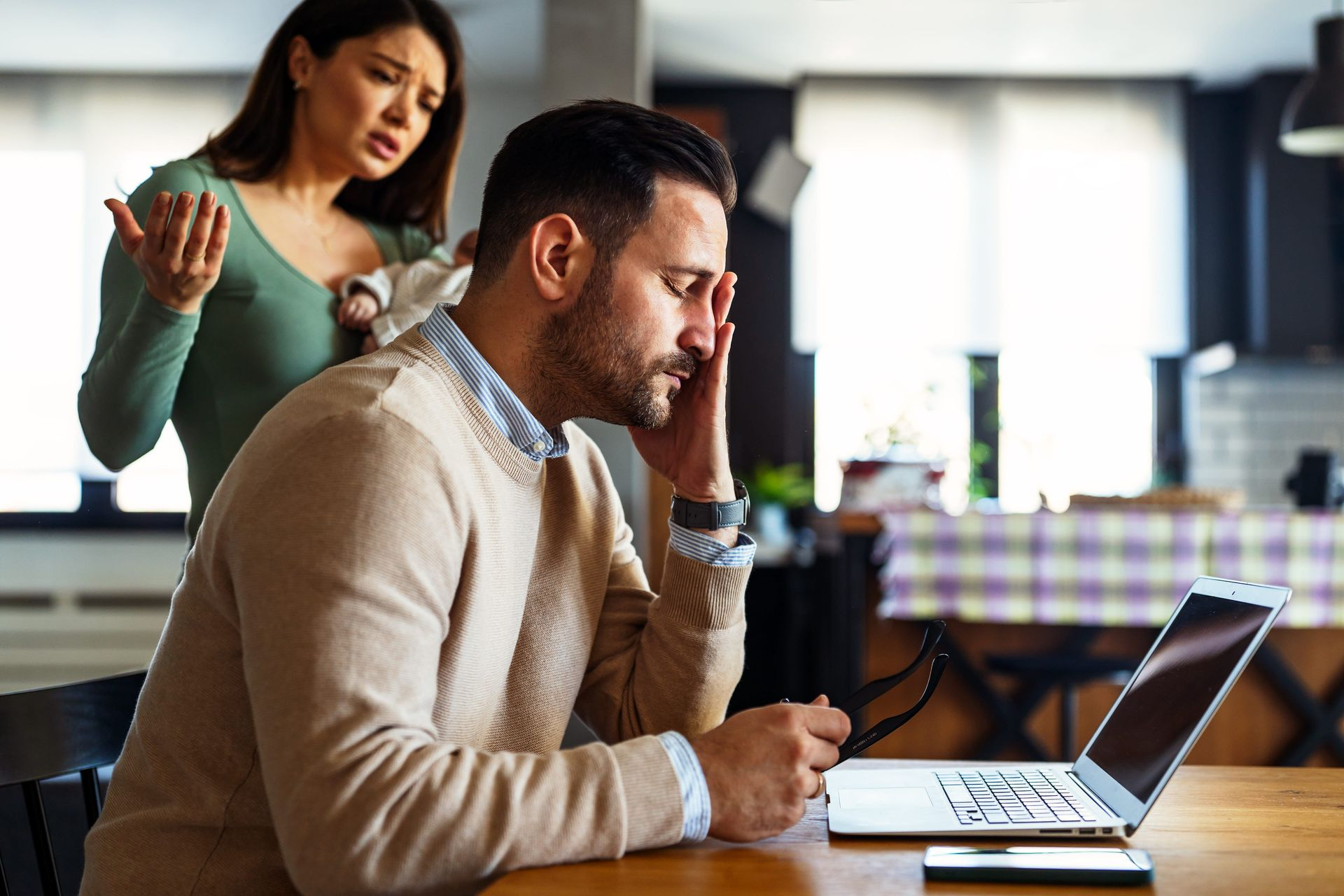 Office worker typing at a laptop while a colleague stands behind him, gesturing in discussion