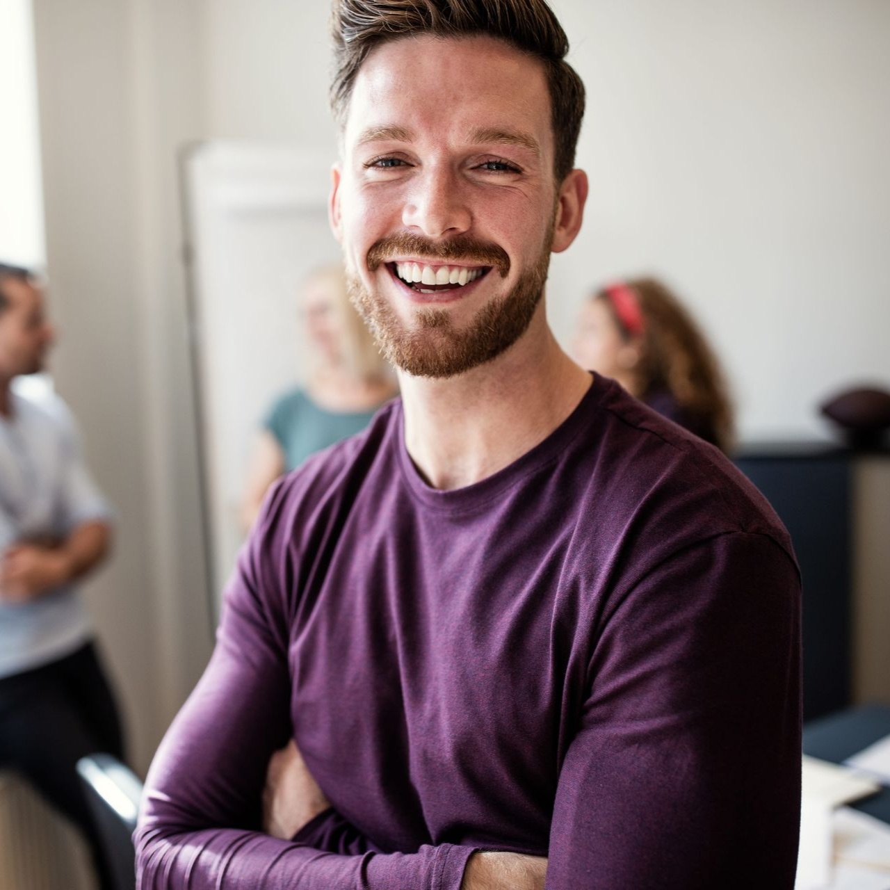Smiling man in a purple shirt with arms crossed in an office setting