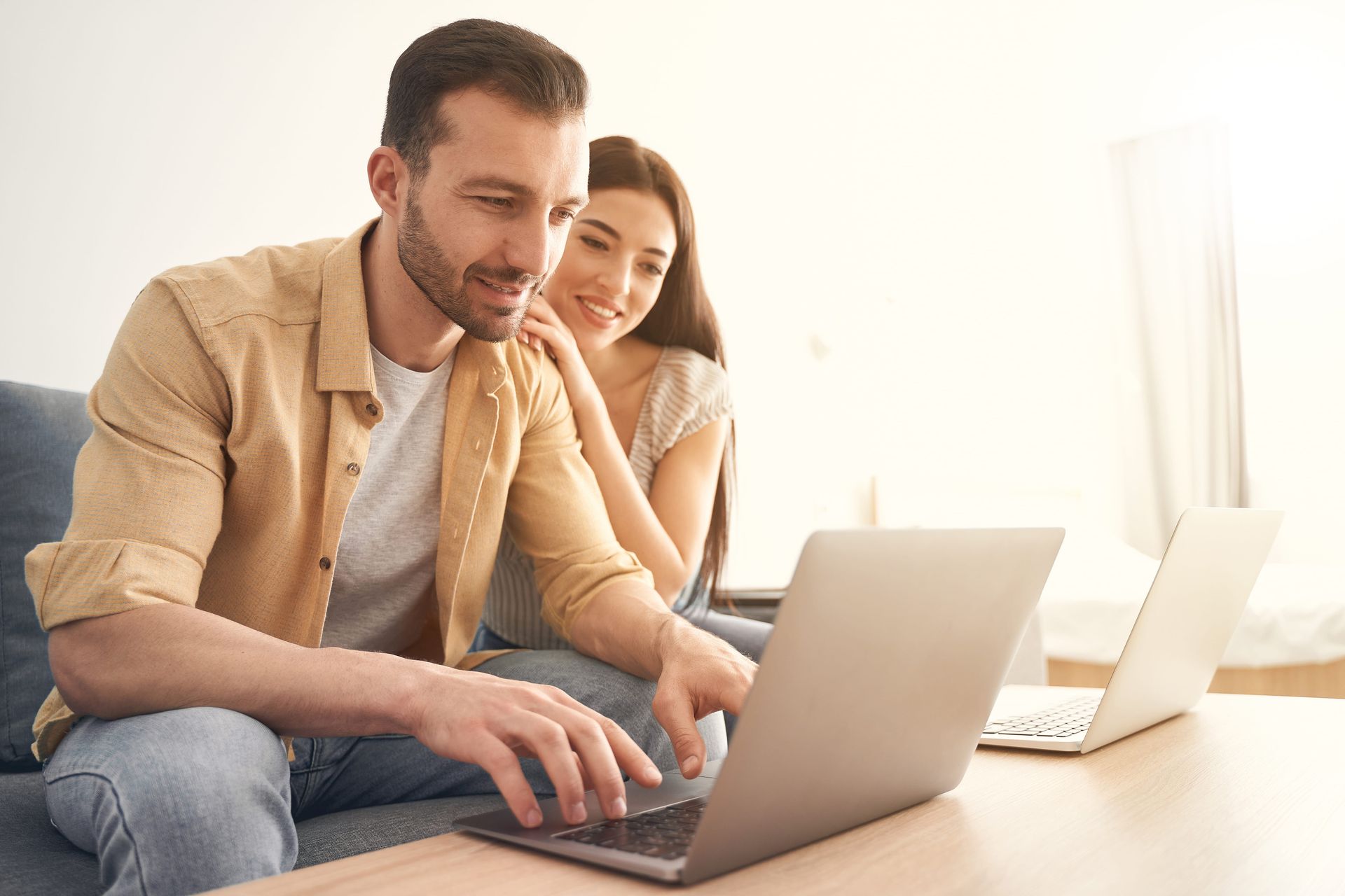 Two people working on laptops at a bright desk, smiling and collaborating in a home office