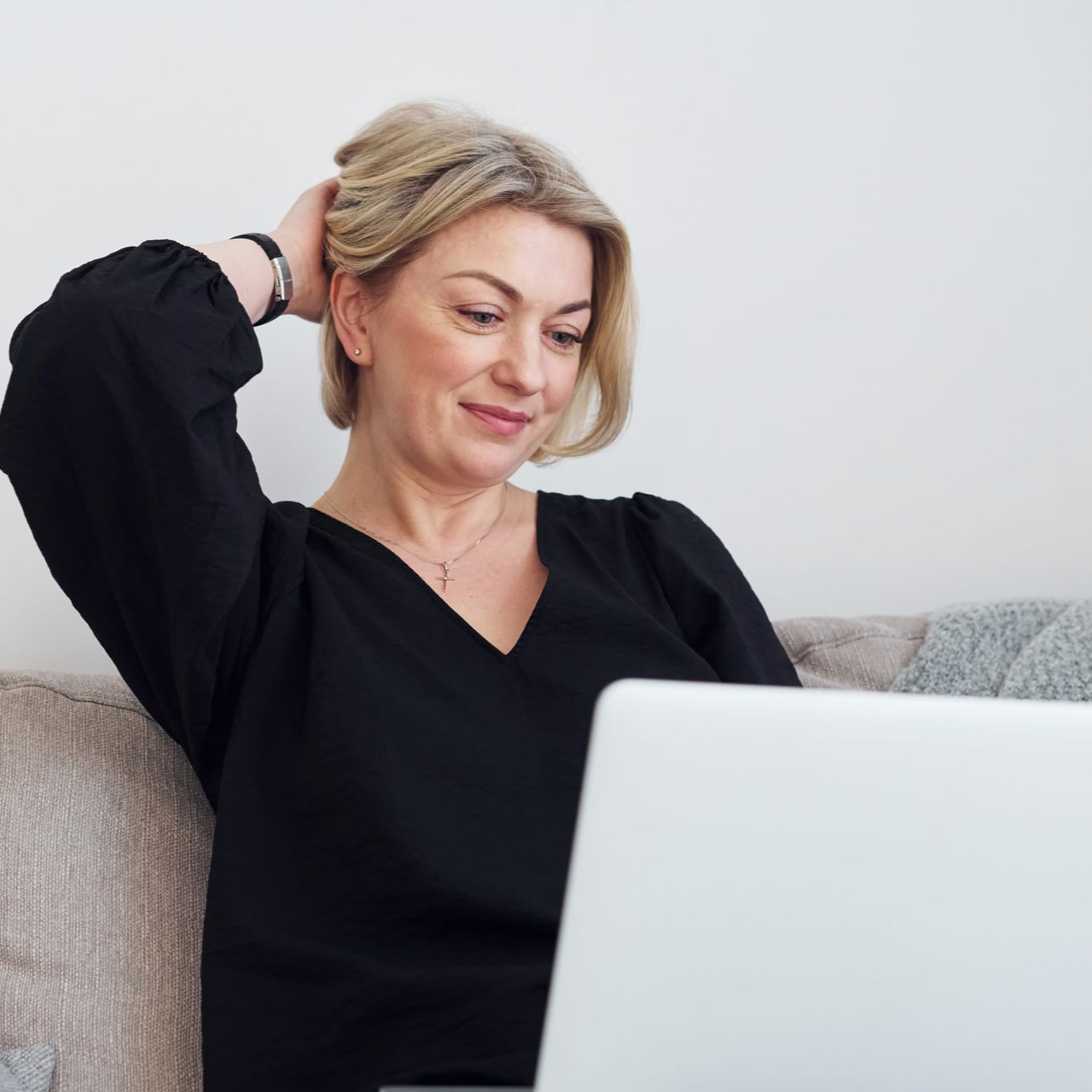 Person sitting on a couch, looking at a laptop with one hand behind their head