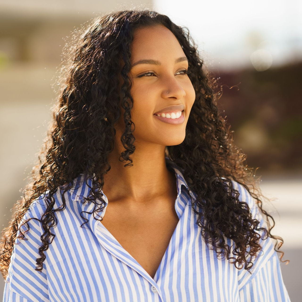 Smiling woman in a blue striped shirt outdoors in sunlight