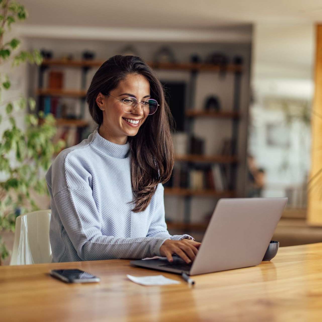 Woman smiling while typing on a laptop at a wooden table in a bright home office
