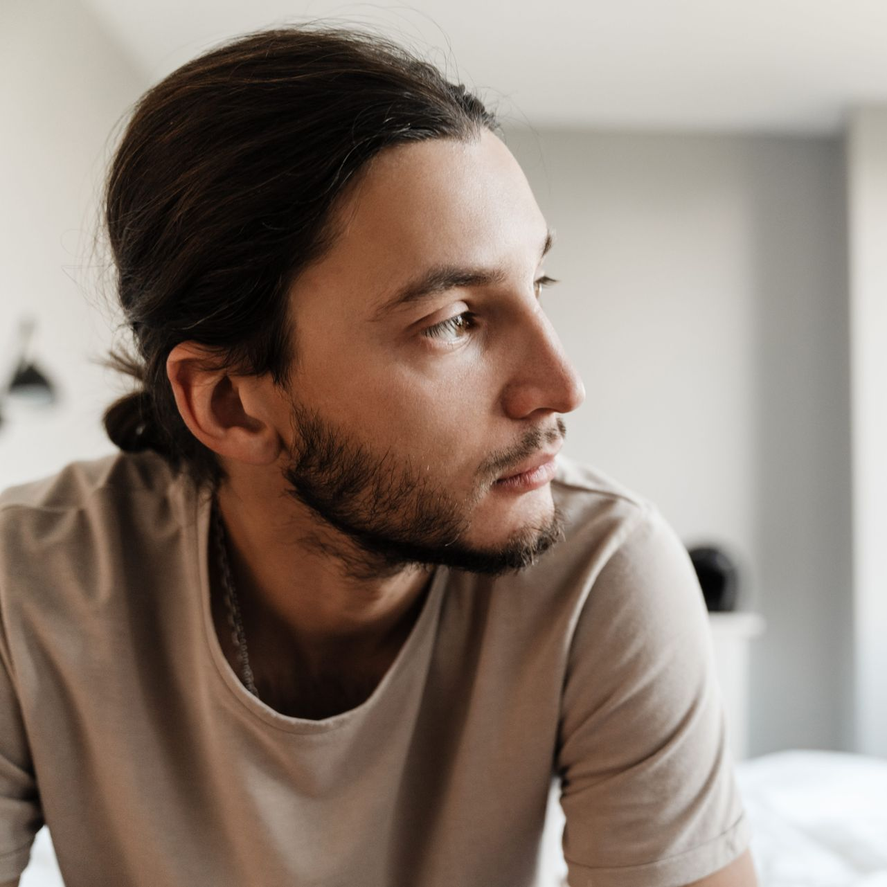 Person in a beige shirt looking out a window with a thoughtful expression