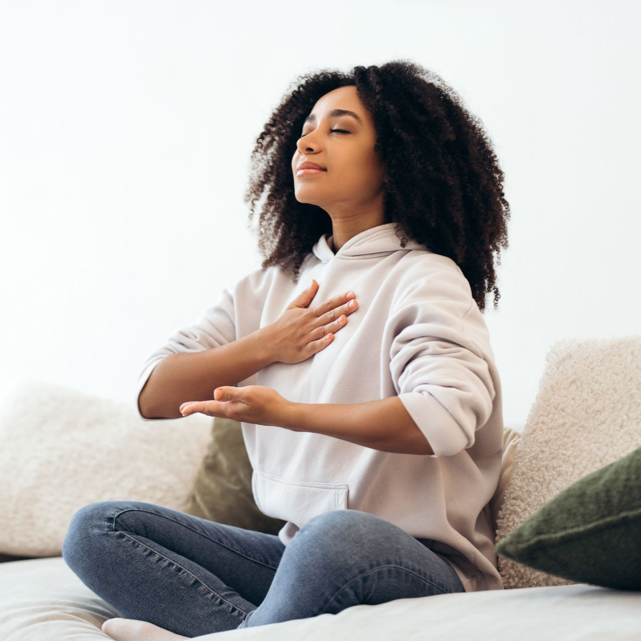 Person meditating cross-legged on a couch, hand on chest, in a bright room
