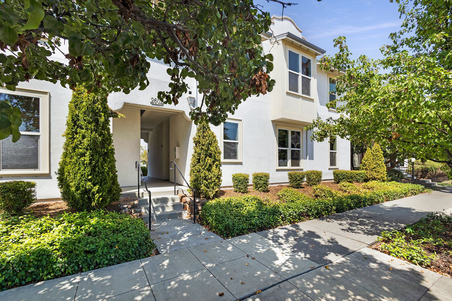 Exterior photo of an apartment building shaded by trees