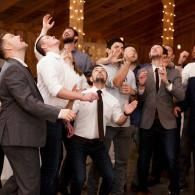 People in suits looking up and reaching at a celebration with warm string lights